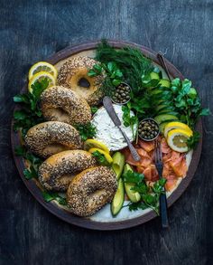 a plate with bagels, cucumbers, lemons and herbs