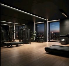 an empty gym with lots of equipment in the room at night, and large windows overlooking city lights