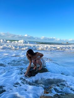 a woman kneeling down on top of a rock in the ocean next to water and waves