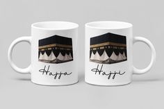 two white coffee mugs with the words happy hajjra written on them