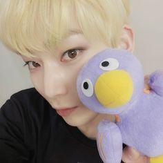 a person holding a purple stuffed animal in their right hand and looking at the camera