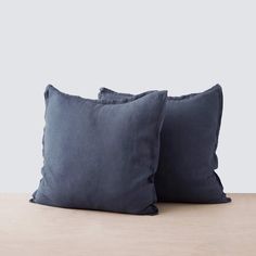 two dark blue pillows sitting on top of a wooden table in front of a white wall