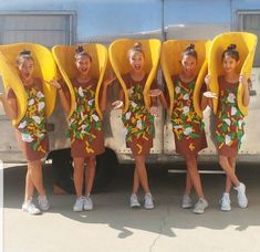 five girls in matching outfits with bananas on their heads and arms, posing for the camera