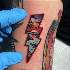 a person with blue gloves on their hands is holding up a tattoo that has an image of a lightning