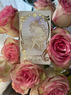 some pink roses are in front of a tarot card with an image of a fairy on it