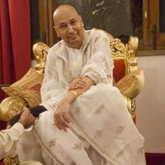 a man sitting on top of a golden chair next to another man in white clothing