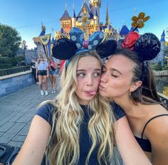 two women kissing each other in front of a castle with mickey mouse ears on their heads