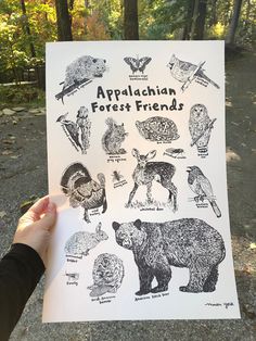 a person holding up a poster with animals on it in front of some trees and leaves