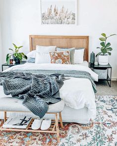 a bedroom with a bed, rugs and plants on the side tables in front of it