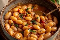 a close up of a bowl of food with beans and herbs in it on a wooden table