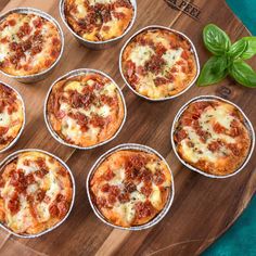 six mini pizzas sitting on top of a wooden cutting board next to basil leaves