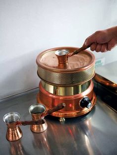 a person is stirring something in a pot on a stove top with copper pans