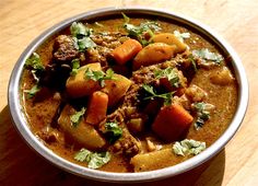 a bowl filled with stew and vegetables on top of a wooden table