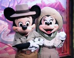 two mickey and minnie mouse characters standing next to each other in front of a backdrop