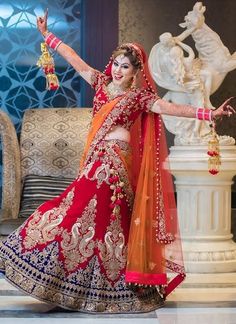 a woman in a red and orange bridal outfit posing with her arms out to the side