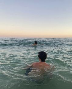 two people swimming in the ocean at sunset