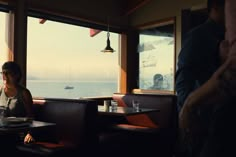 a woman sitting at a table in front of a window looking out on the ocean