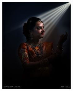 a woman in an orange sari is holding her hand up to the light coming from behind