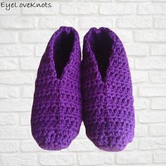 purple crocheted slippers hanging on a brick wall in front of a white brick wall