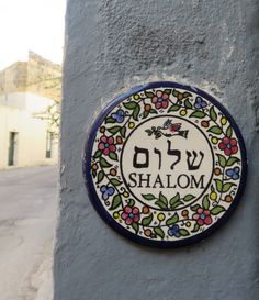 a sign on the side of a building that says shalom in hebrew and has flowers around it