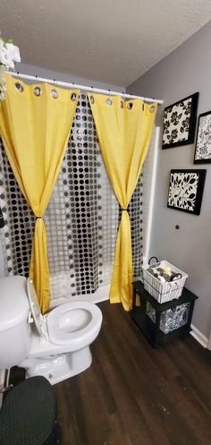 a white toilet sitting next to a window covered in yellow curtains and black and white pictures