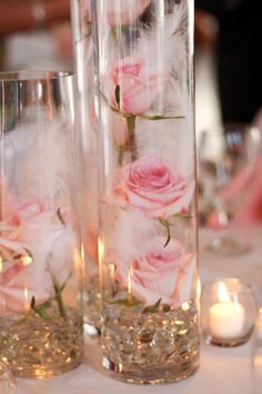 two tall vases filled with pink roses and feathers on top of a white table