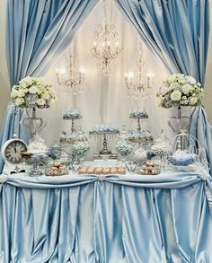 a table topped with lots of desserts under a chandelier covered in blue drapes