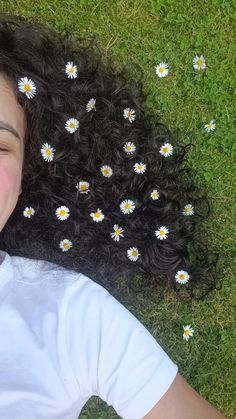 a woman laying in the grass with daisies on her hair