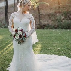 a woman in a white wedding dress standing on the grass with her arms around her waist