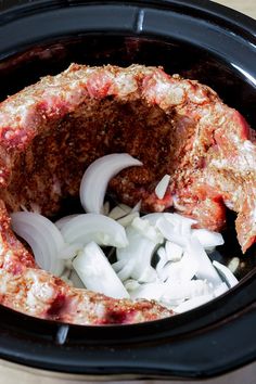 an open crock pot with onions and meat in it