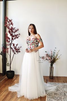 a woman standing in front of a white wall wearing a dress with flowers on it