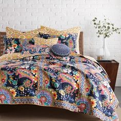 a bed covered in a blue paisley comforter next to a white brick wall