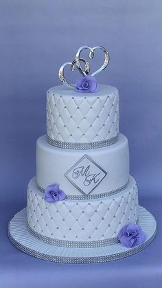 a three tiered wedding cake with purple flowers on the top and initials on the bottom