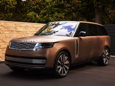 the new range rover is parked in front of a stone wall with trees behind it