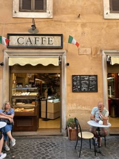 two people sitting at tables in front of a cafe