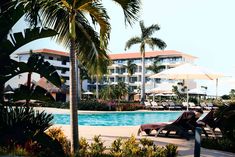 an outdoor swimming pool with lounge chairs and umbrellas next to the resort's main building