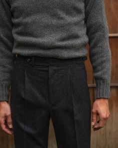 a man standing in front of a wooden wall wearing a sweater and pants with buttons