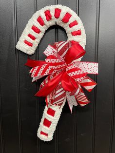 a red and white christmas wreath hanging on the front door with ribbon attached to it