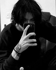 black and white photograph of a person holding up a cell phone to their face while sitting in a chair