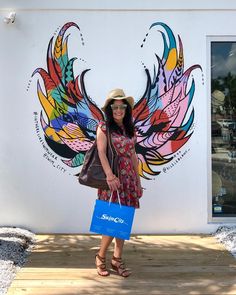 a woman standing in front of a building with a colorful mural on the wall behind her