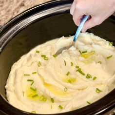 a person is spooning mashed potatoes in a crock pot with green onions