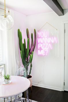 a pink neon sign that says you wanna pizza next to a cactus in a vase