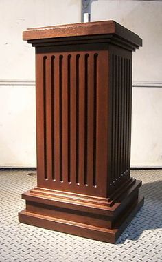 a wooden trash can sitting on top of a tiled floor next to a white wall