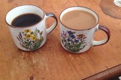 two coffee mugs sitting on top of a wooden table with flowers painted on them