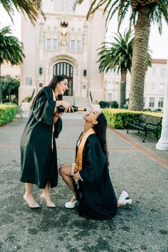 two women in graduation gowns sitting on the ground and one is brushing her teeth