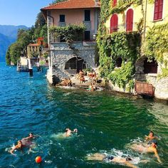 people swimming in the water next to buildings and trees on both sides of the lake