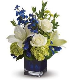 blue and white flowers in a square vase with greenery on the side, including roses