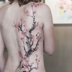 the back of a woman's body with flowers painted on it and branches in bloom