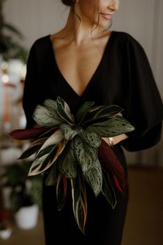 a woman wearing a black dress holding a green and red flower