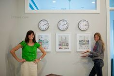 two women standing next to each other in front of clocks and pictures on the wall